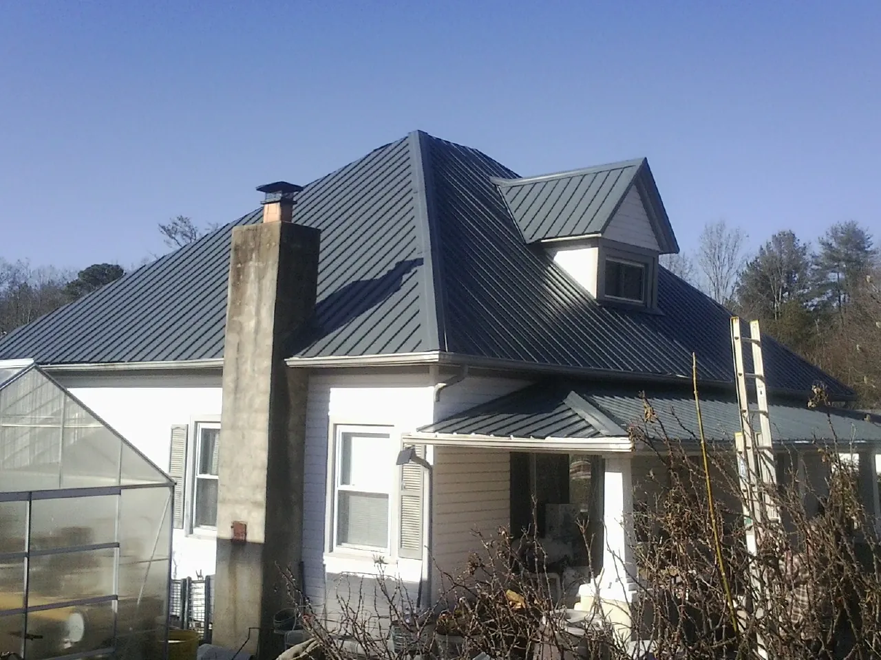Dark blue standing seam metal roof on a white farmhouse with dormer — Slate & Tile Roof Repair by Roofing Brothers in Wilmont