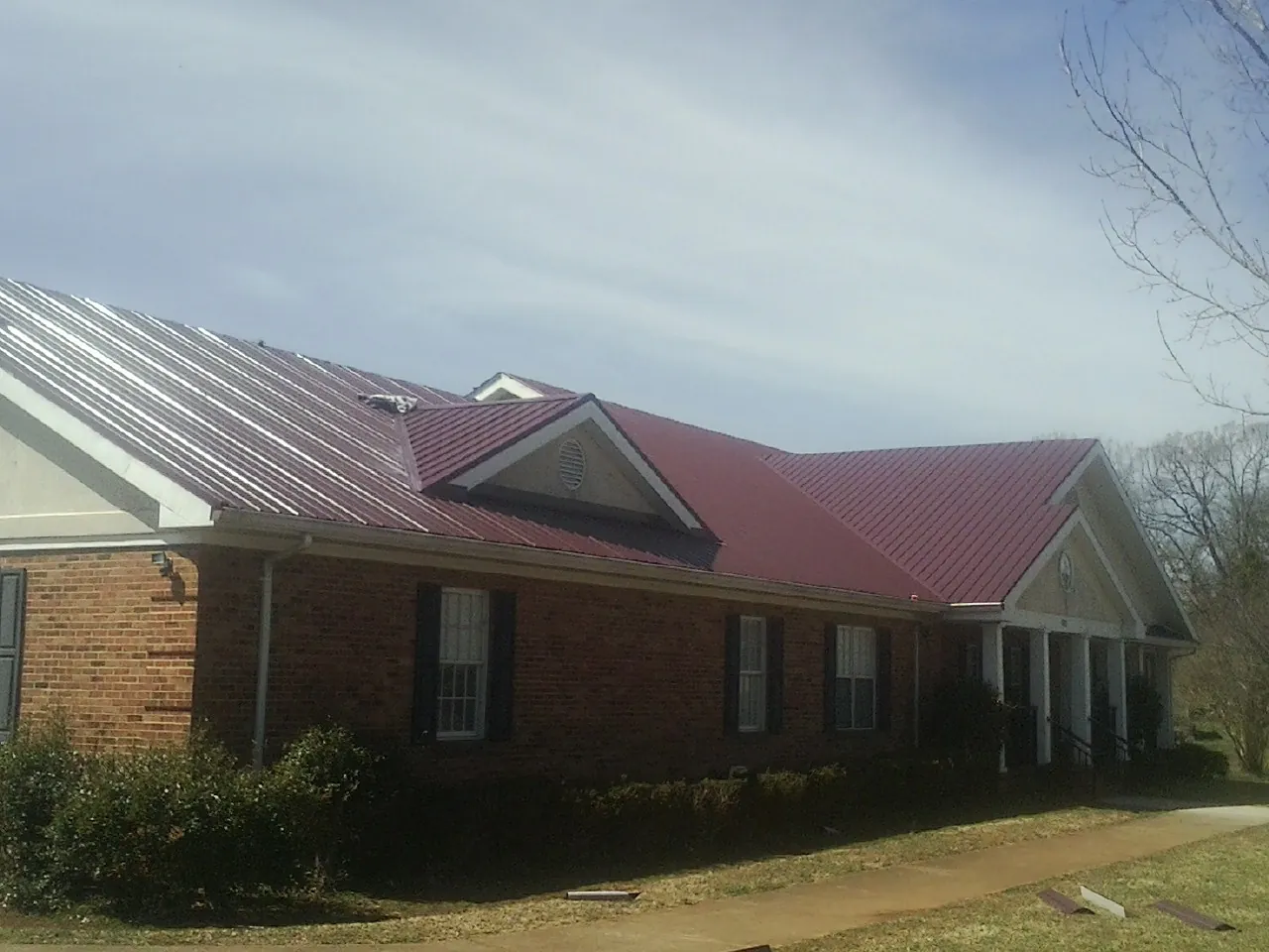 Red metal roof with gabled entries on a long brick building, from a Hail Damage Roof Repair job in Wilmont