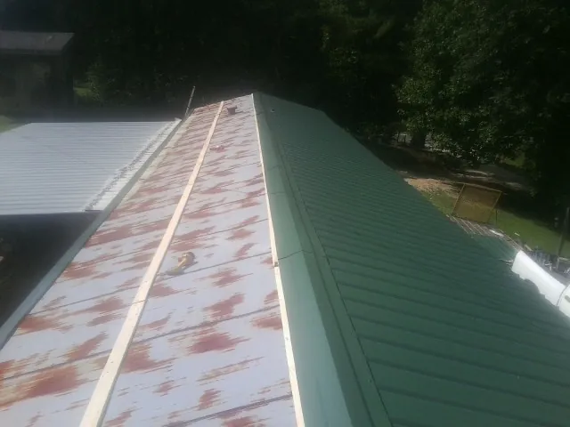 Old rusted panels beside newly installed green metal roofing — Wind Damage Roof Repair by Roofing Brothers in Wilmont
