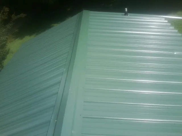 New green metal panels meeting at the ridge of a roof — Flat Roof Repair work by our crew in Wilmont