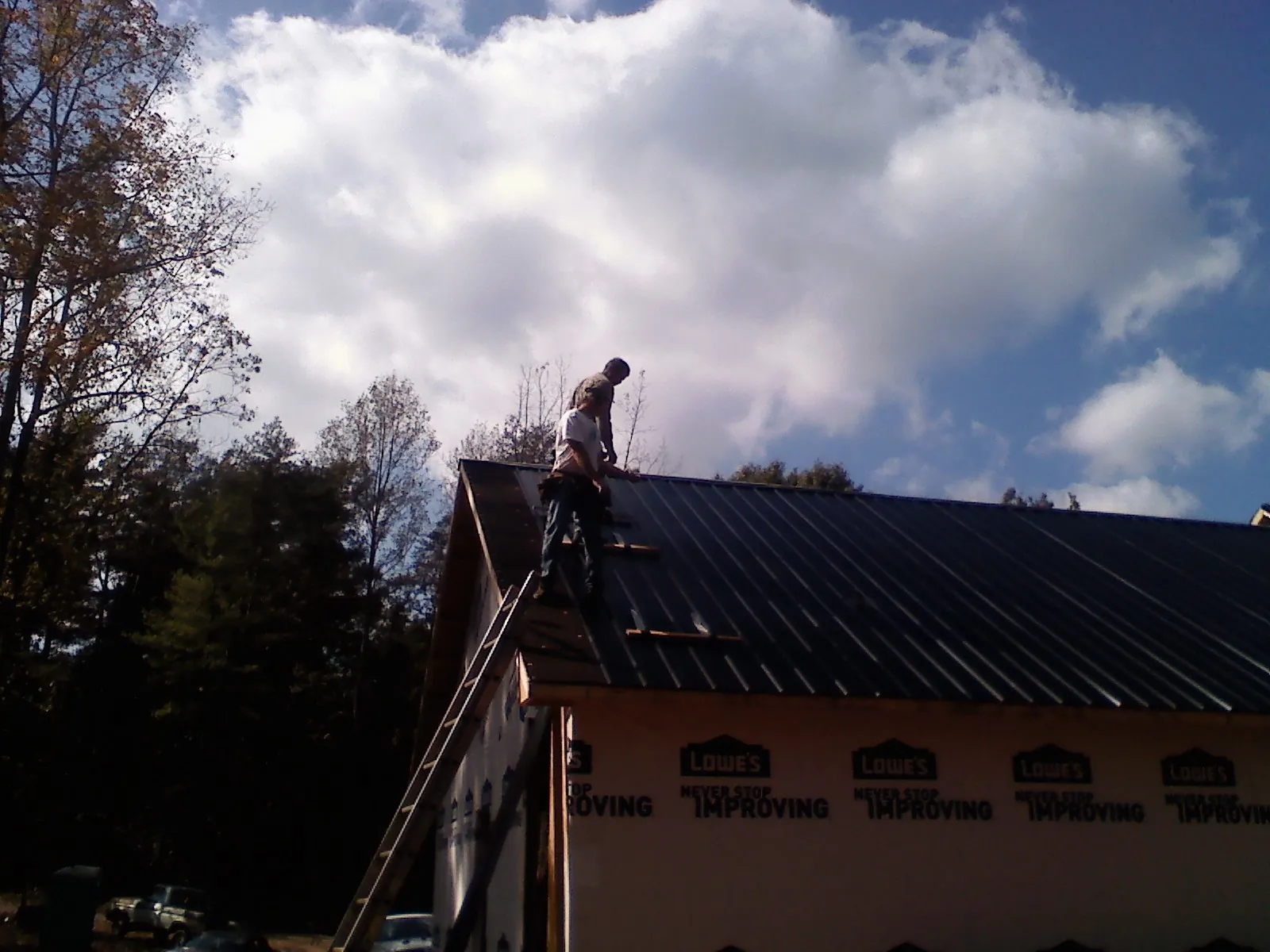 Roofer fastening dark metal panels high against a cloudy sky, from a Roof Inspection job in Wilmont