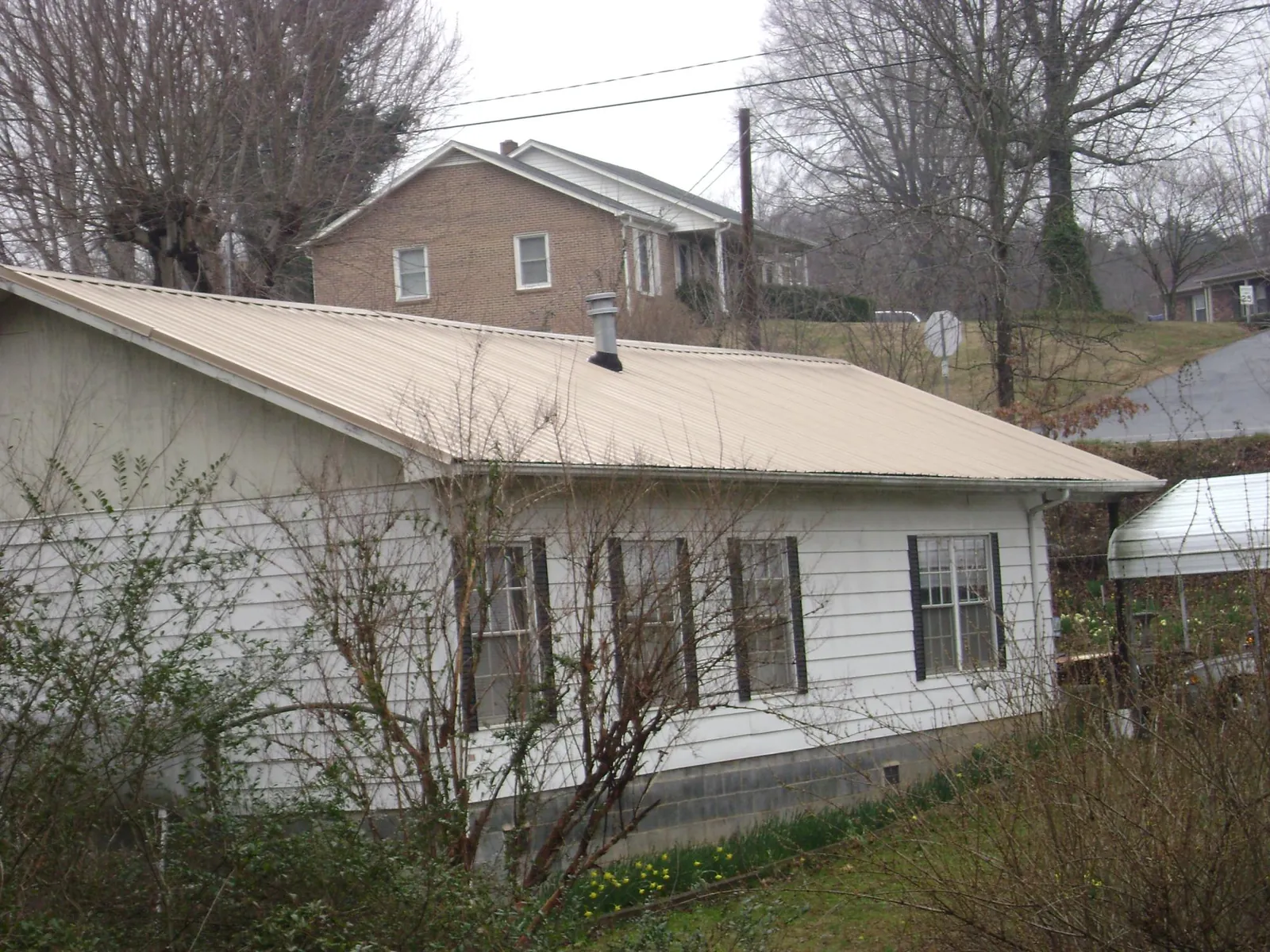 Tan metal roof on a white sided house set into a hillside — Commercial Roofing by Roofing Brothers in Wilmont