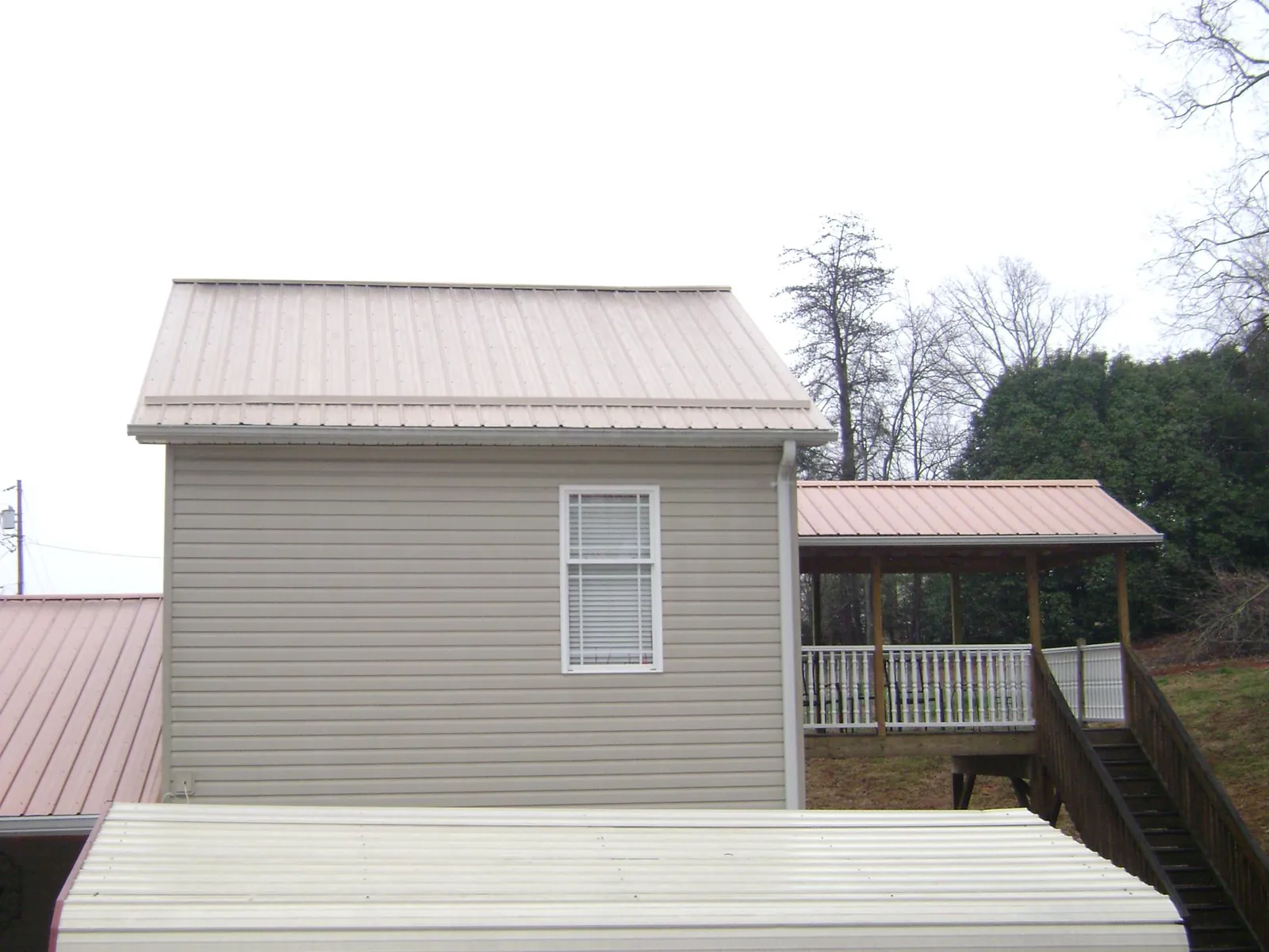 Tan metal roofs on a two story addition and attached porch, from a Roof Replacement job in Wilmont