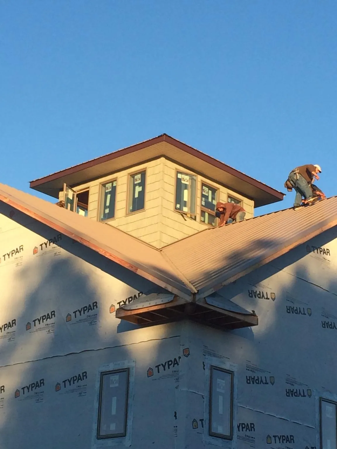 Roofers working around a rooftop cupola on a new metal roof at sunset — Roof Waterproofing in Wilmont by Roofing Brothers